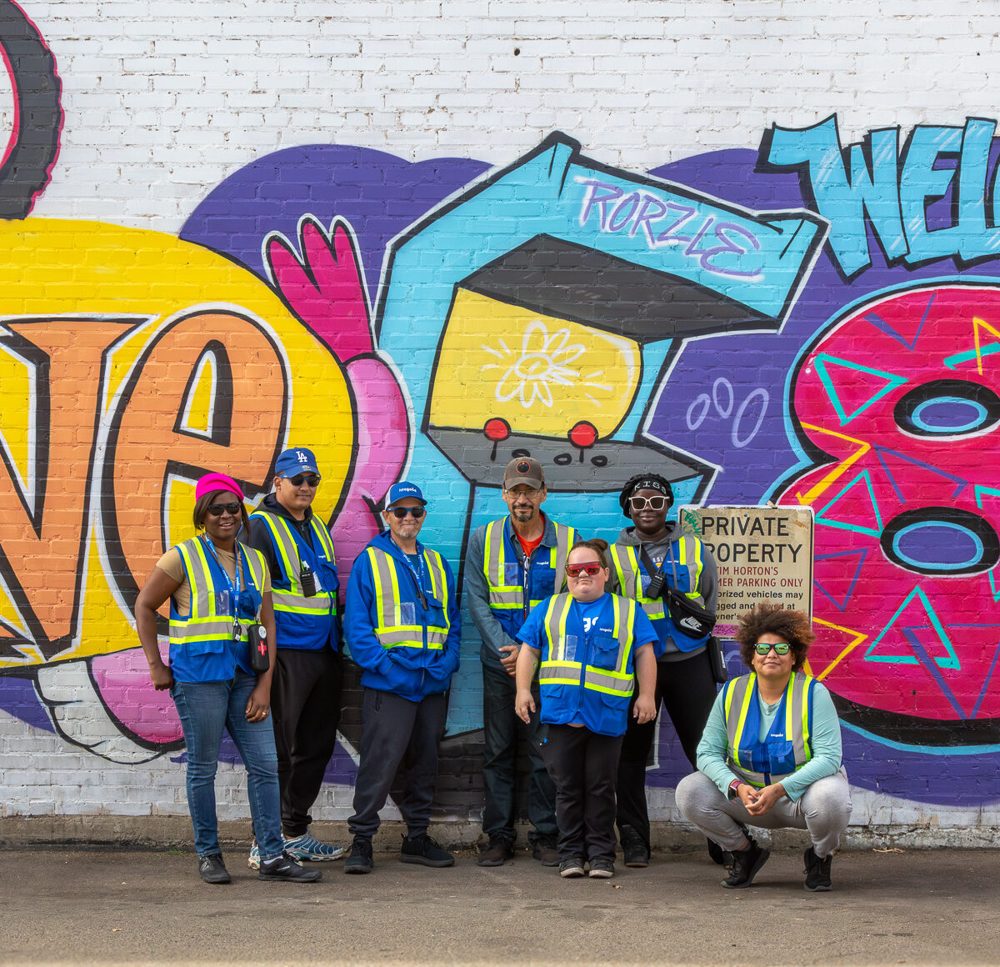 Team in safety vests in front of a welcome mural in Old Strathcona
