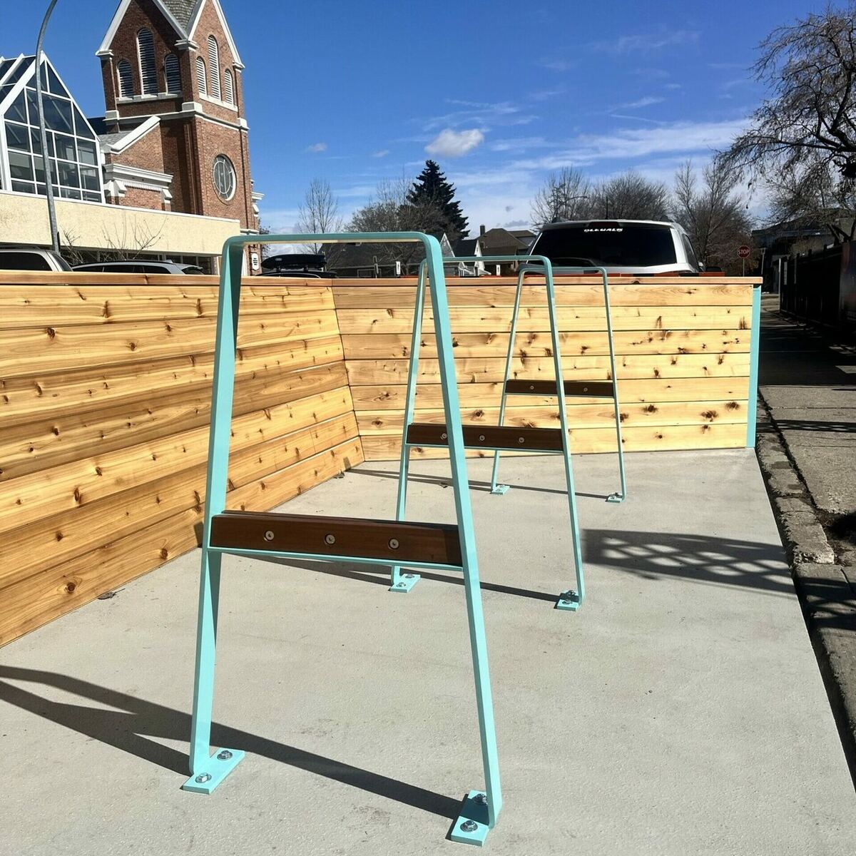 Teal A-frame bike racks with wood seat rails installed on a downtown Edmonton sidewalk